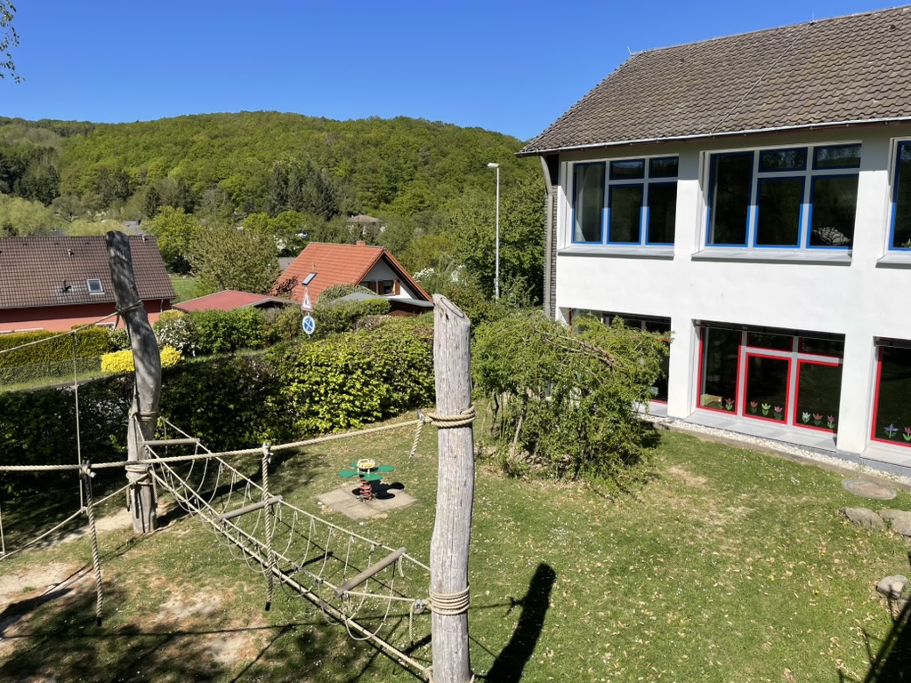 Das Gebäude der Regenbogenschule Schalkenbach, davor das Seilspielgerät, dahinter der bewaldete Hang des Brohltals