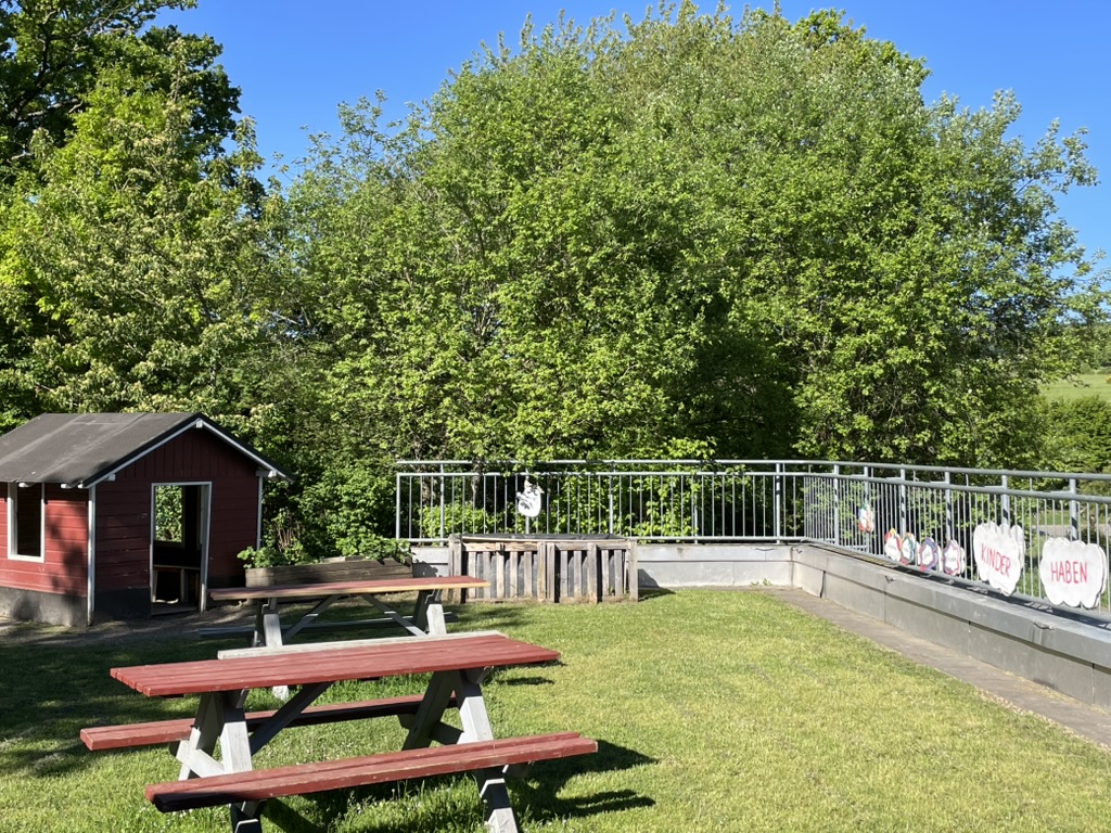 Schulgarten mit Picknickbänken und rotem Gerätehäuschen
