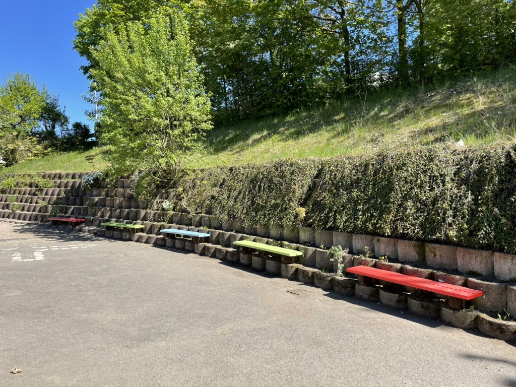 Bunte Sitzbänke am Hang neben der Schule